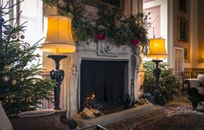 Main Hall lit fireplace with christmas trees and festive decorations.